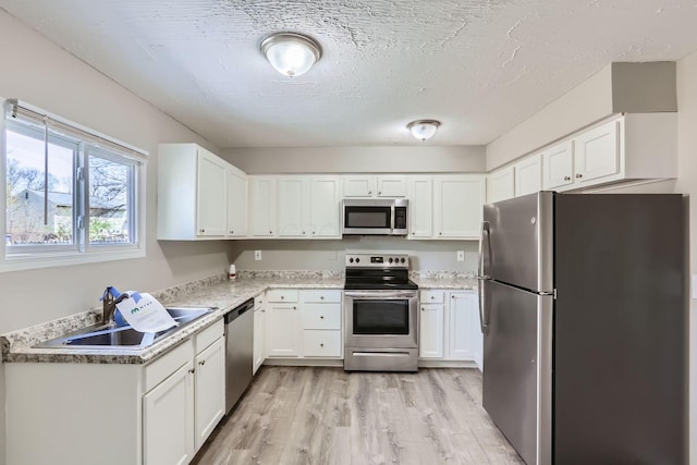 kitchen with light wood finished floors, stainless steel appliances, a textured ceiling, a sink, and white cabinetry