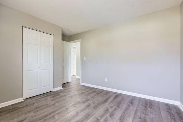 unfurnished bedroom with baseboards, wood finished floors, and a closet