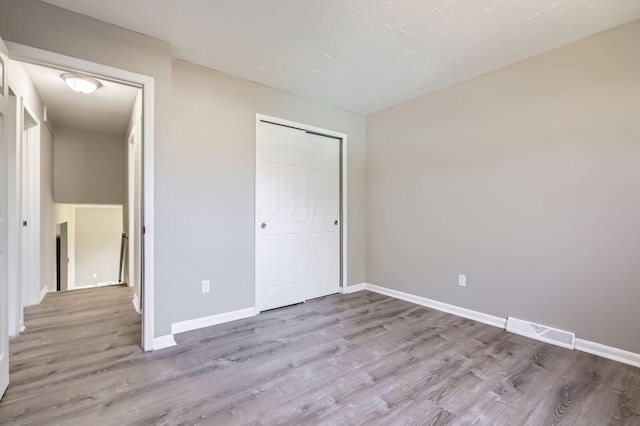 unfurnished bedroom with a closet, wood finished floors, visible vents, and baseboards