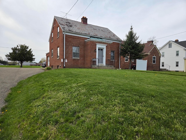 view of front of property with brick siding, a high end roof, a front lawn, and a chimney