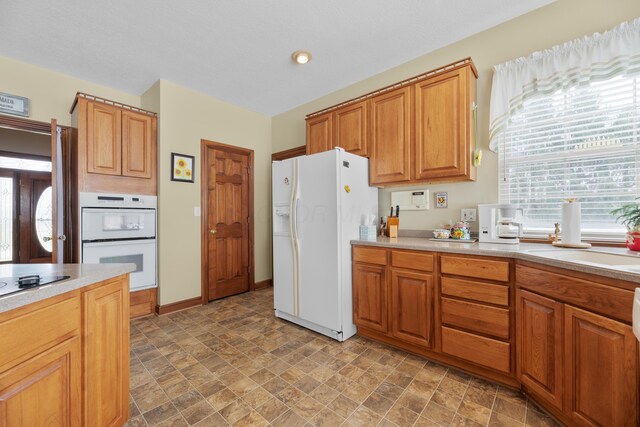 kitchen featuring baseboards, light countertops, white appliances, and stone finish flooring