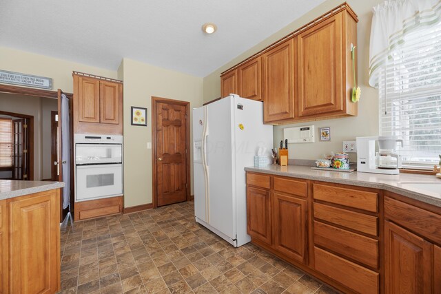 kitchen with light countertops, brown cabinetry, stone finish floor, and white appliances