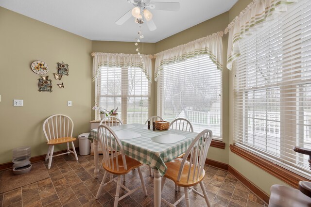 dining space with baseboards, a ceiling fan, and stone finish flooring