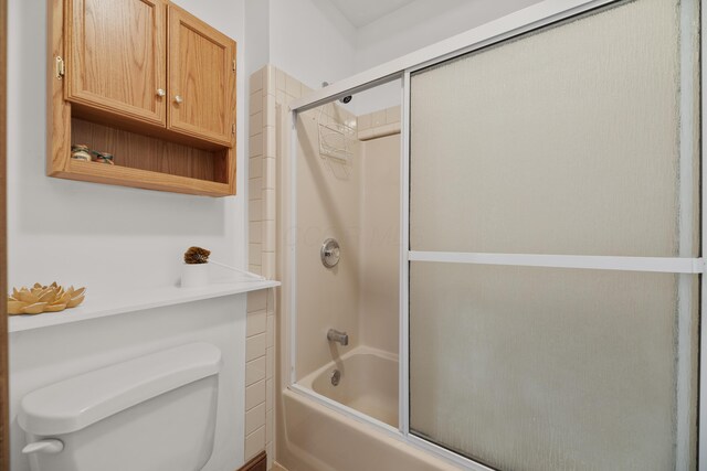 bathroom with toilet and shower / bath combination with glass door