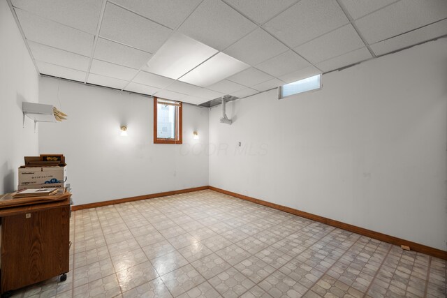 basement with a drop ceiling, baseboards, and light floors