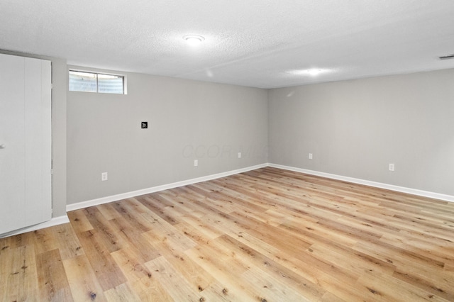 below grade area with light wood-style flooring, a textured ceiling, and baseboards