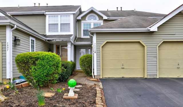 townhome / multi-family property with a garage, driveway, and roof with shingles