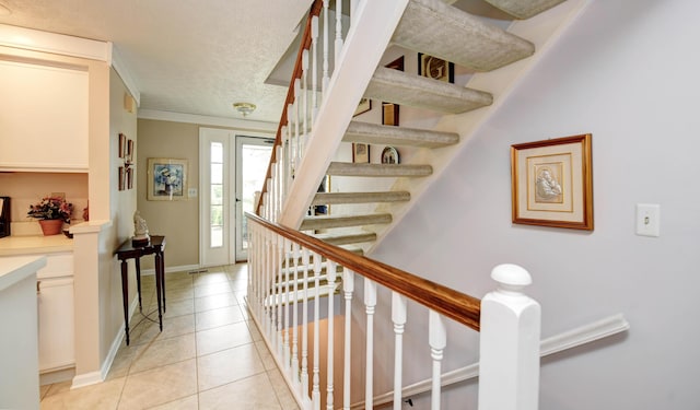 stairway with tile patterned floors, baseboards, a textured ceiling, and ornamental molding