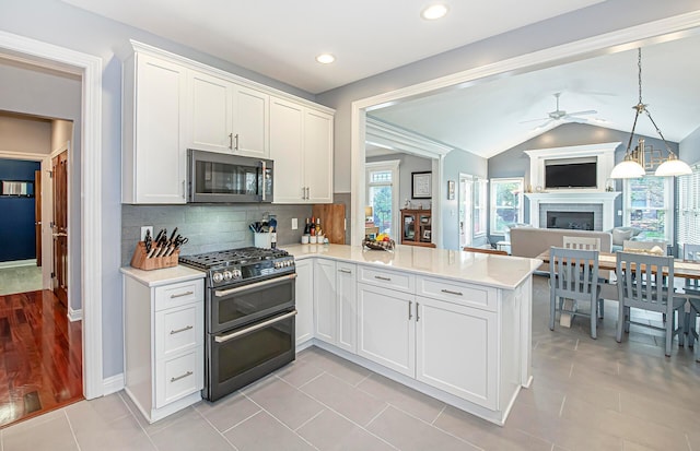 kitchen with a fireplace, a ceiling fan, stainless steel microwave, light countertops, and range with two ovens