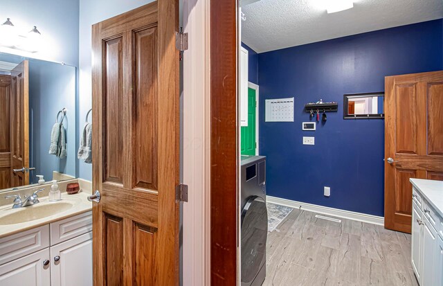 bathroom with washer / clothes dryer, a textured ceiling, vanity, wood finished floors, and baseboards