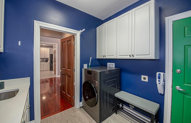 clothes washing area with light wood-type flooring, a textured ceiling, a sink, washer / dryer, and cabinet space