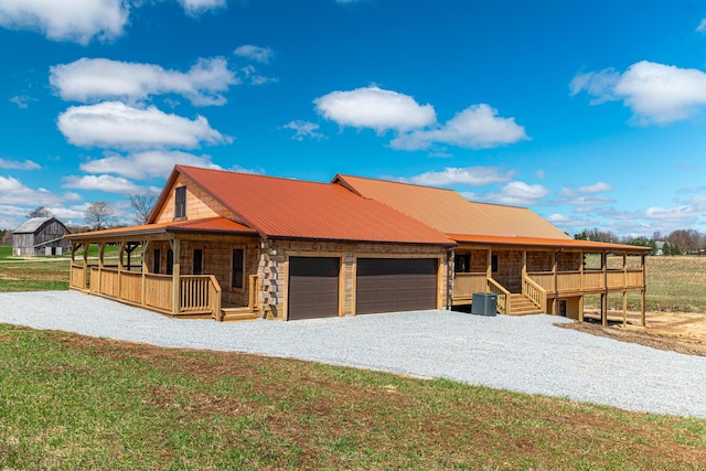 view of front facade with central air condition unit, a porch, metal roof, an attached garage, and driveway