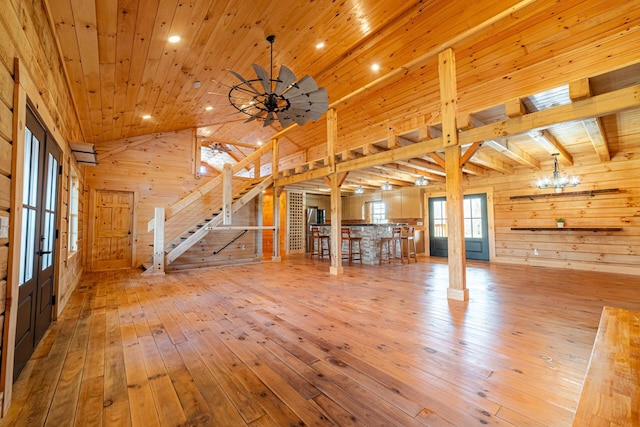 unfurnished living room with wood walls, hardwood / wood-style flooring, wood ceiling, stairs, and french doors