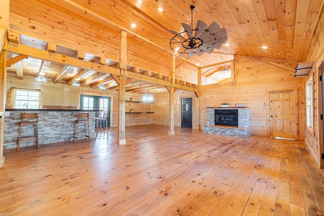 unfurnished living room featuring a stone fireplace, wood walls, hardwood / wood-style floors, high vaulted ceiling, and wooden ceiling