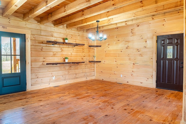 entrance foyer featuring wooden walls, beam ceiling, light wood finished floors, and an inviting chandelier