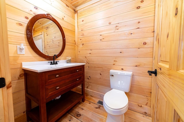bathroom featuring wooden walls, vanity, toilet, and wood finished floors