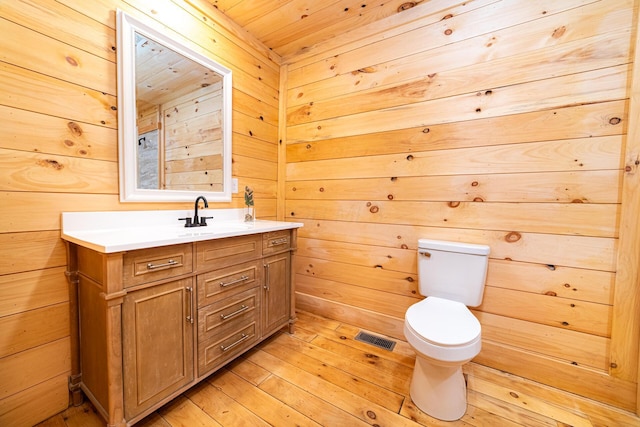 bathroom featuring visible vents, toilet, hardwood / wood-style flooring, vanity, and wood walls