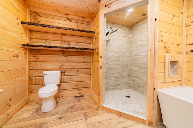 bathroom with wood walls, toilet, a stall shower, and wood finished floors