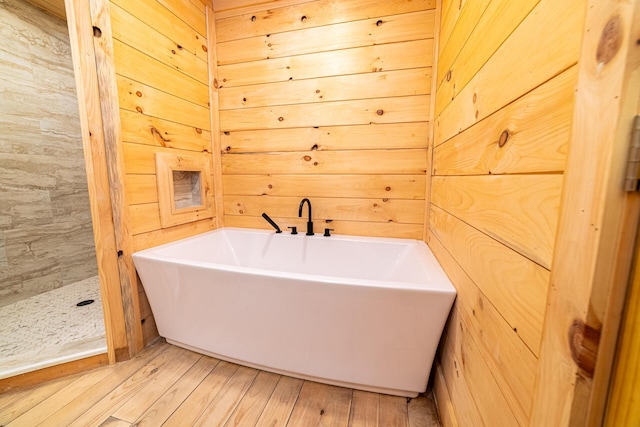 bathroom with a soaking tub, wood finished floors, wood walls, and tiled shower