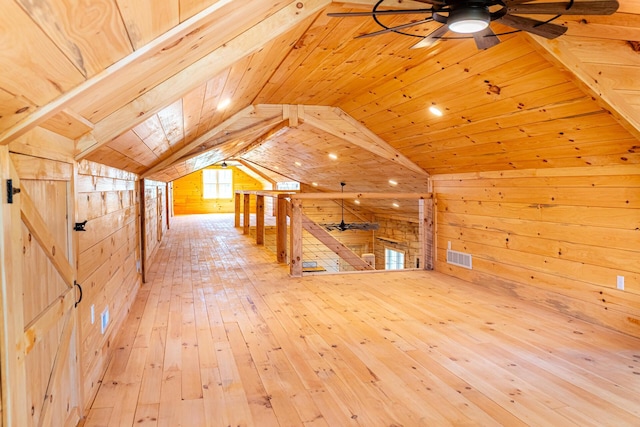 additional living space with visible vents, ceiling fan, hardwood / wood-style flooring, wooden walls, and vaulted ceiling