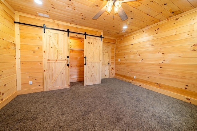 unfurnished bedroom with a barn door, wood ceiling, wooden walls, and carpet floors