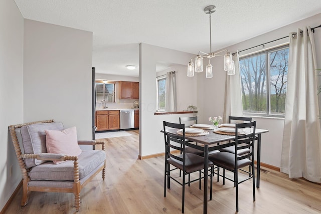 1581 Ringfield Dr, Galloway, OH 43119 - dining space featuring a chandelier, light wood-style flooring, baseboards, and a textured ceiling