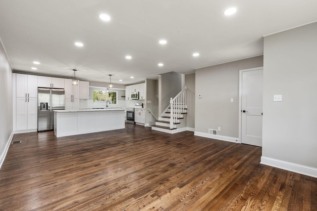 unfurnished living room featuring recessed lighting, dark wood-type flooring, baseboards, and stairs