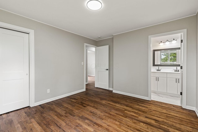 unfurnished bedroom with dark wood finished floors, crown molding, baseboards, connected bathroom, and a sink