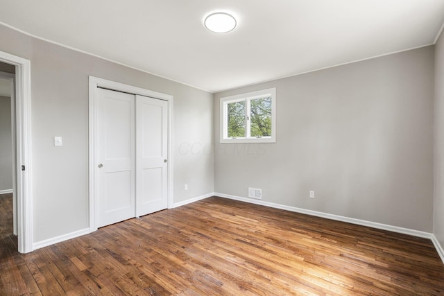 unfurnished bedroom featuring wood finished floors, baseboards, and a closet