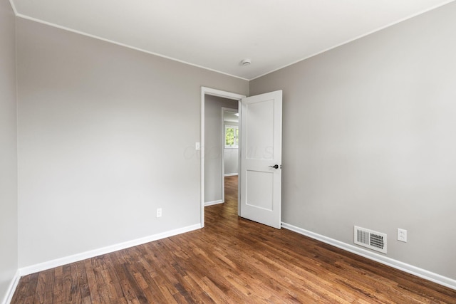empty room featuring baseboards, wood finished floors, ornamental molding, and a smoke detector