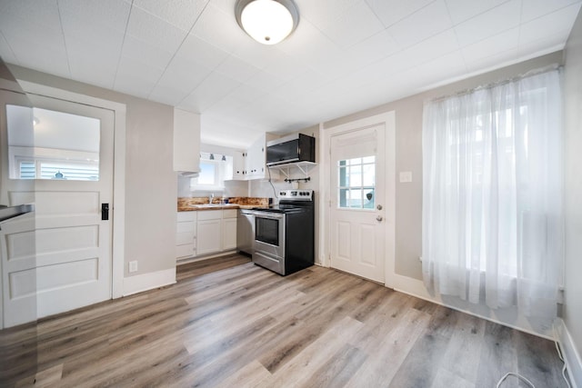 kitchen featuring white cabinets, a sink, stainless steel electric range, light wood finished floors, and baseboards