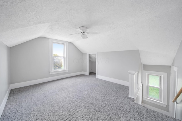 bonus room with baseboards, vaulted ceiling, a textured ceiling, a ceiling fan, and carpet