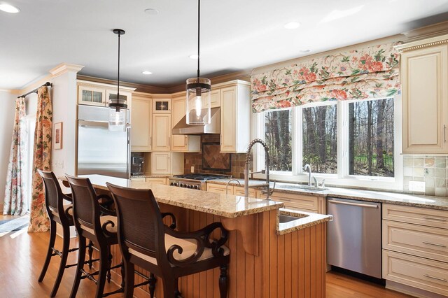 6795 Macneil Dr, Dublin, OH 43017 - kitchen featuring tasteful backsplash, light stone counters, cream cabinetry, wall chimney exhaust hood, and appliances with stainless steel finishes