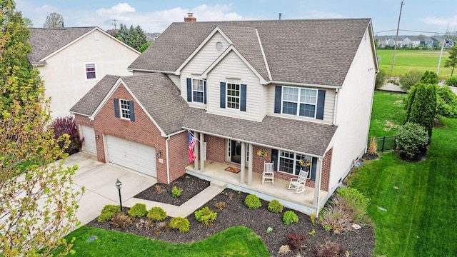 traditional-style home with roof with shingles, covered porch, a front yard, and brick siding