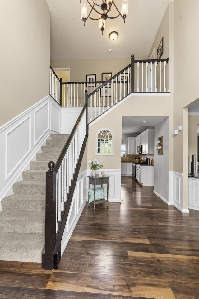 stairway with wainscoting, wood finished floors, a decorative wall, a high ceiling, and a chandelier