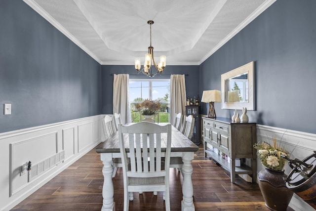dining space with dark wood-style flooring, a raised ceiling, a wainscoted wall, an inviting chandelier, and ornamental molding