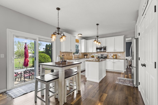 kitchen featuring a kitchen island, backsplash, appliances with stainless steel finishes, an inviting chandelier, and white cabinetry