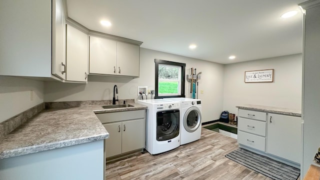 clothes washing area featuring recessed lighting, washing machine and dryer, light wood-style flooring, cabinet space, and a sink
