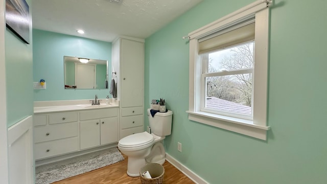 bathroom with toilet, vanity, wood finished floors, and baseboards