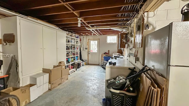 below grade area featuring freestanding refrigerator and concrete block wall