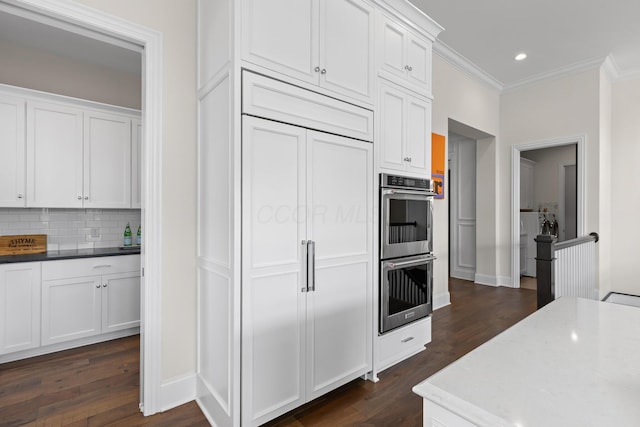 kitchen featuring dark wood finished floors, double oven, backsplash, ornamental molding, and white cabinetry
