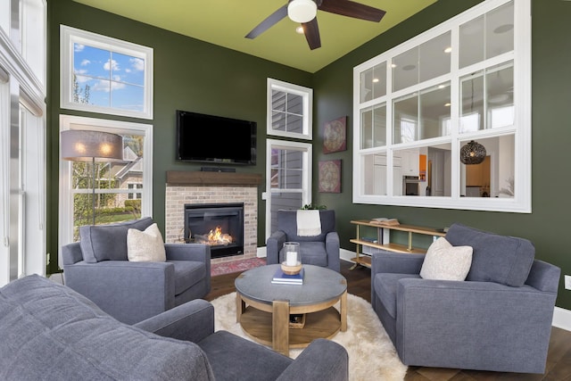 living area featuring baseboards, a ceiling fan, wood finished floors, and a fireplace