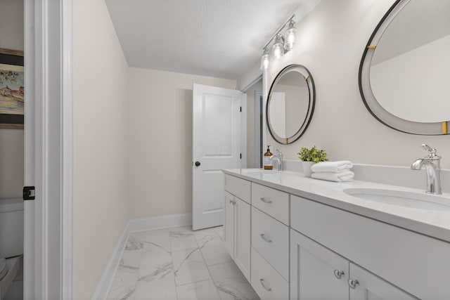 full bathroom with double vanity, marble finish floor, baseboards, and a sink