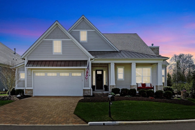 craftsman inspired home featuring decorative driveway, stone siding, a porch, a front yard, and a standing seam roof
