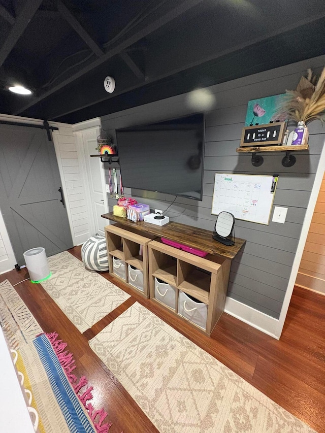 bedroom with wood walls, baseboards, a barn door, and wood finished floors