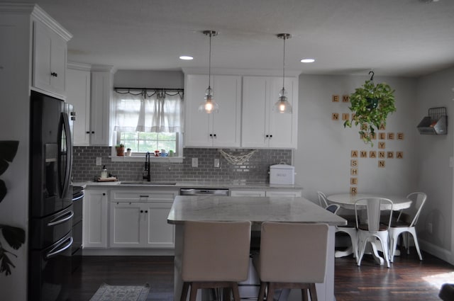 kitchen featuring dark wood-style flooring, light stone counters, freestanding refrigerator, backsplash, and a sink