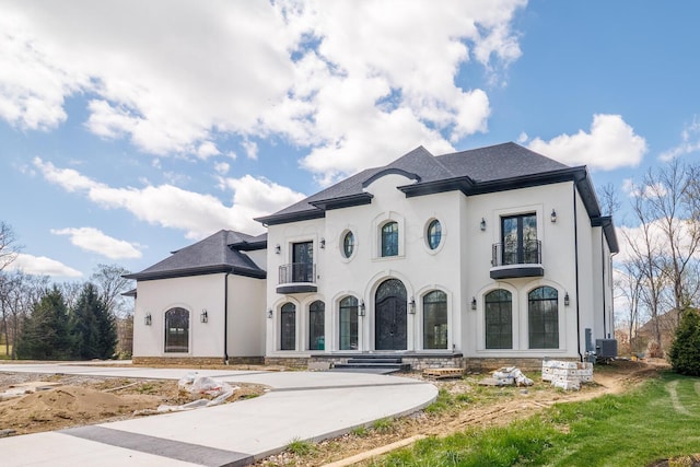 french country inspired facade featuring central AC unit, a balcony, and stucco siding