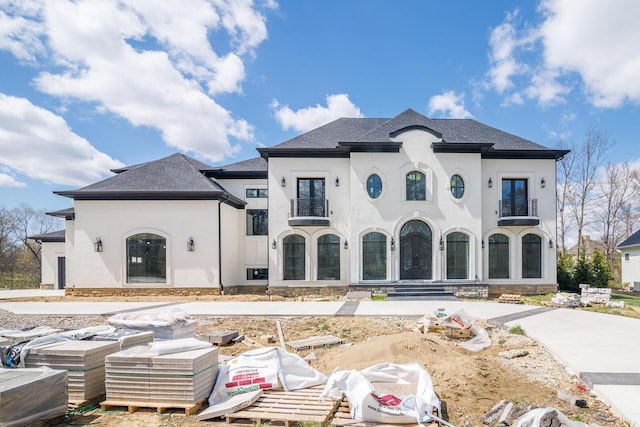 french country style house with roof with shingles, stucco siding, and a balcony