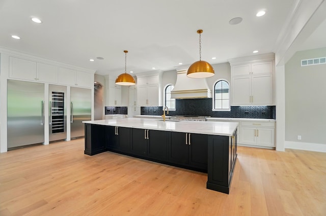 10007 Allen Dr, Dublin, OH 43017 - kitchen with custom exhaust hood, white cabinetry, dark cabinetry, decorative backsplash, and light wood finished floors