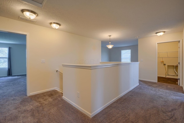 hallway with dark carpet, visible vents, baseboards, and an upstairs landing